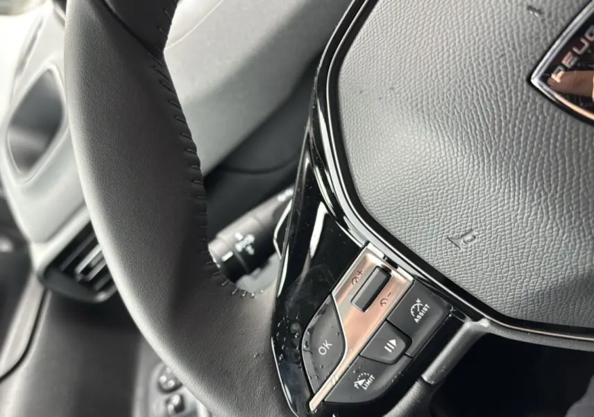 Gros plan sur le volant cuir multifonctions du Peugeot Rifter gris artense, mettant en valeur les commandes au volant.