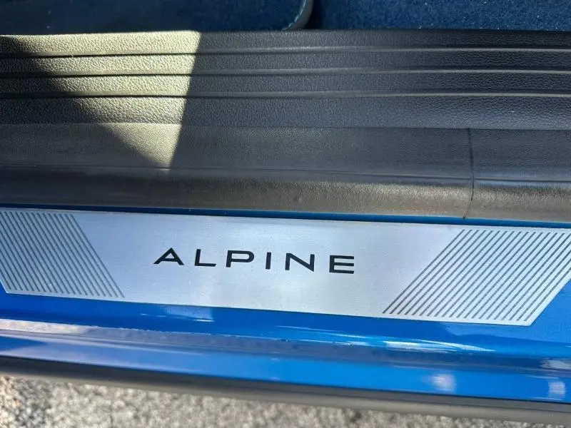Gros plan sur la plaque de seuil de porte "ALPINE" avec la carrosserie Bleu Sommet métallisé visible en dessous.
