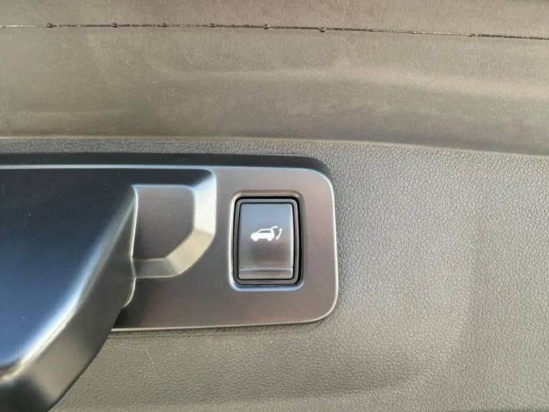 Gros plan sur le bouton d'ouverture électrique du coffre dans l'habitacle du Renault Rafale bleu sommet métallisé.