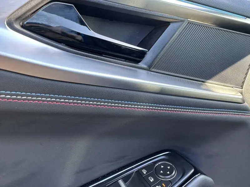 Détail de la porte intérieure côté gauche du Renault Rafale 2025 bleu sommet, avec surpiqûres tricolores et commandes électriques.