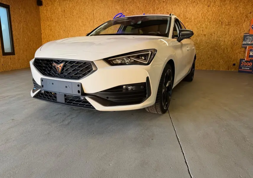 Vue 3/4 avant droite d'une CUPRA Leon ST blanche 2024 avec calandre noire et jantes noires en intérieur bois.