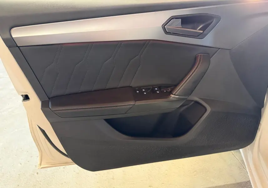 Vue rapprochée de la porte avant gauche noire avec surpiqûres et commandes des vitres d'une CUPRA LEON ST blanche 2024.