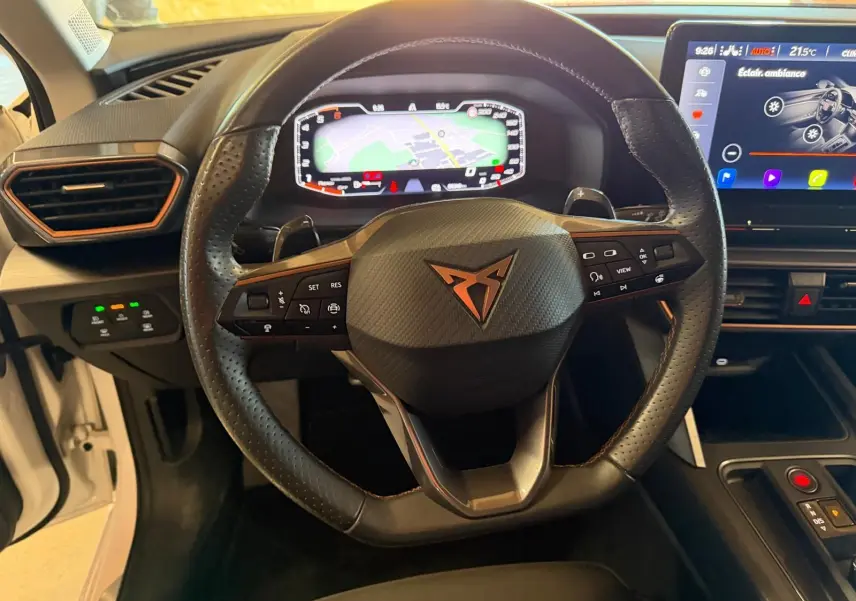 Vue intérieure centrée sur le volant noir perforé avec logo CUPRA et tableau de bord numérique affichant la navigation.