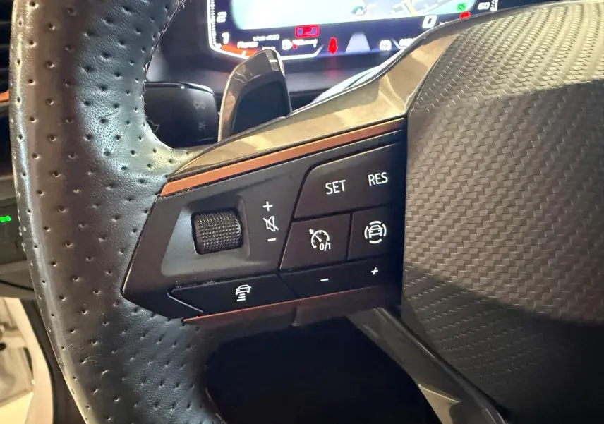 Gros plan sur les commandes de régulateur de vitesse au volant perforé d'une CUPRA LEON ST 2024, intérieur noir.