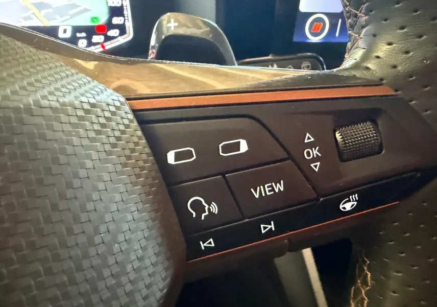 Gros plan sur les commandes du volant en cuir perforé du CUPRA LEON ST 2024, avec touches rétroéclairées et finition carbone.