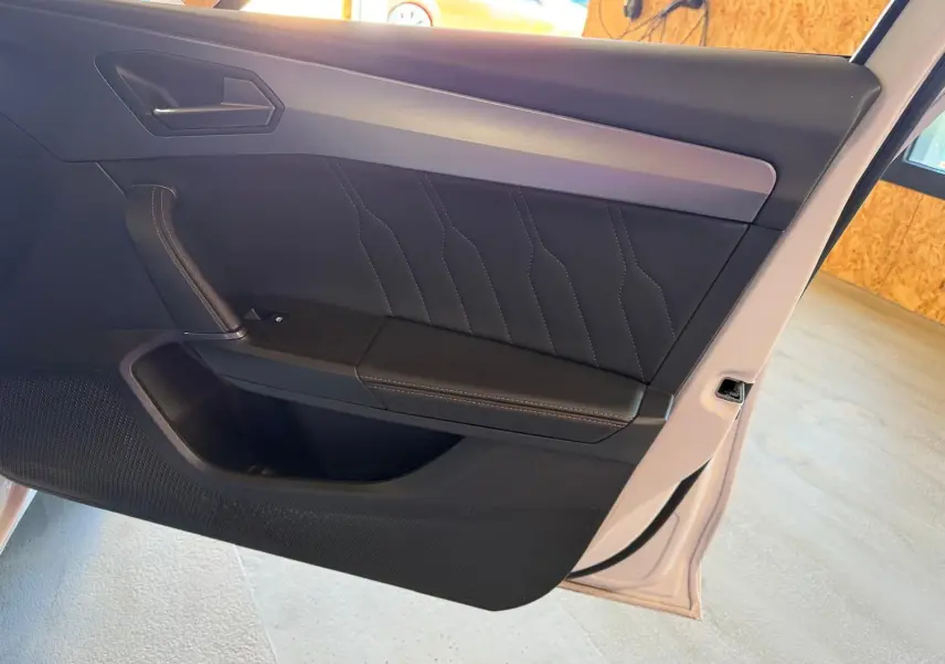 Vue intérieure de la porte avant droite blanche d'une CUPRA LEON ST 2024 avec garniture noire et surpiqûres contrastées.
