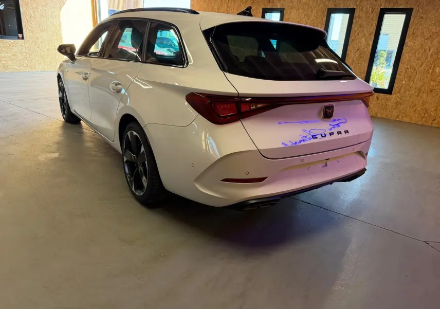 Vue 3/4 arrière droite d'une CUPRA LEON ST blanche 2024 avec feux arrière reliés et jantes noires distinctives.