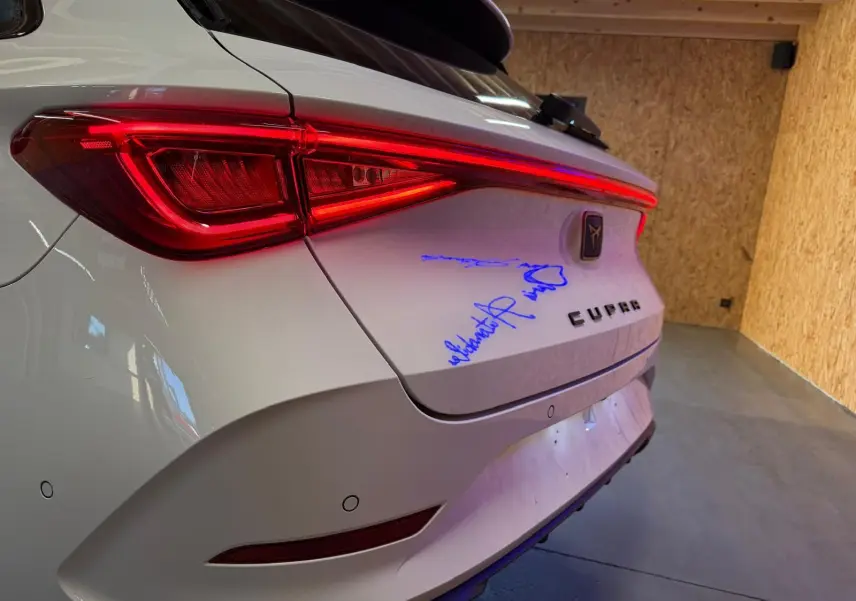 Vue arrière droite d'une CUPRA LEON ST blanche 2024 avec feux LED allumés et signature bleue sur le coffre.