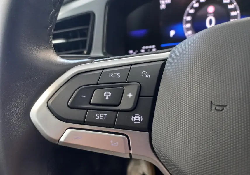 Gros plan sur les commandes au volant côté gauche du Volkswagen T-Roc 2025 gris Indium, avec affichage numérique en arrière-plan.