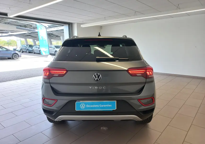 Vue arrière d'un Volkswagen T-Roc gris Indium 2025, avec feux LED allumés et badge T-ROC visible au centre.