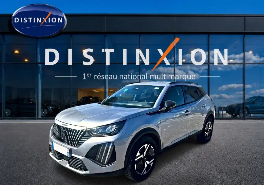 Peugeot 2008 gris artense vue 3/4 avant droit, avec jantes alu et calandre distinctive devant un showroom Distinxion.