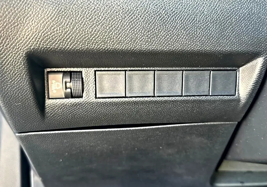 Gros plan sur les commandes de réglage des phares et boutons latéraux dans l'habitacle noir du Peugeot 2008 gris Artense.