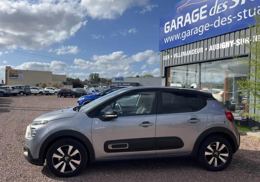 Profil droit d'une Citroën C3 gris nacré 2022 avec toit noir et protections latérales noires sur un parking extérieur.