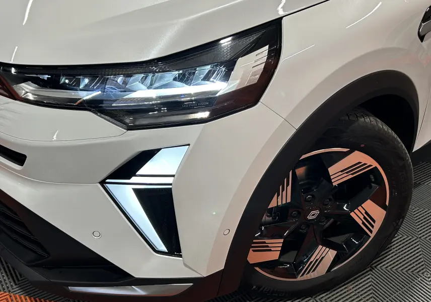 Gros plan sur l'avant droit du Renault SYMBIOZ blanc nacré, mettant en valeur le phare LED et la jante bicolore stylisée.