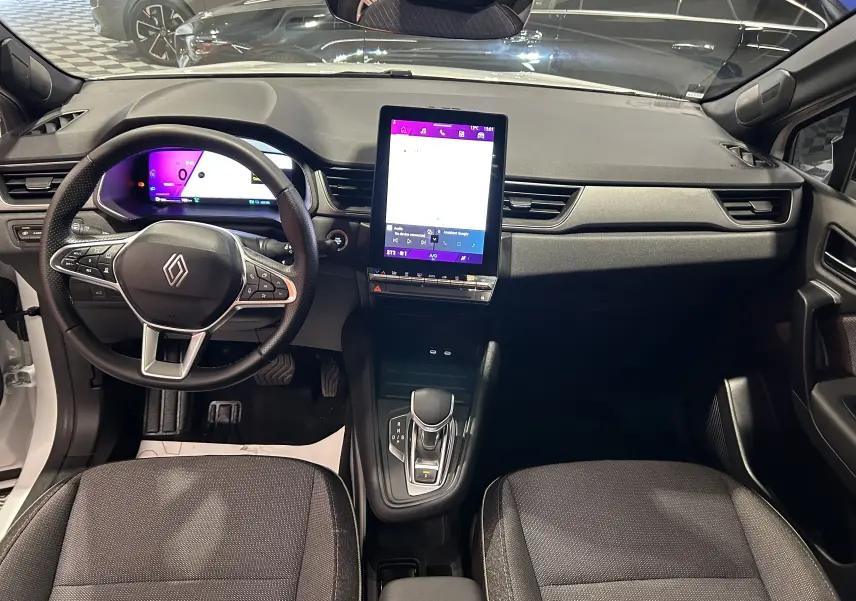 Vue intérieure avant du Renault Symbioz blanc nacré 2025, tableau de bord moderne avec écran tactile vertical et volant multifonction.