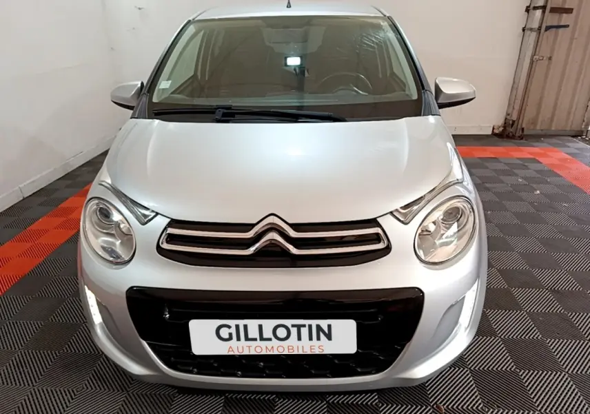 Vue avant d'une Citroën C1 gris clair 2019 avec phares ronds et calandre chromée dans un garage.