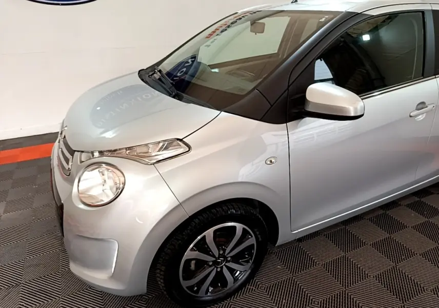 Vue 3/4 avant droit d'une Citroën C1 gris clair avec jantes alliage et rétroviseurs assortis.