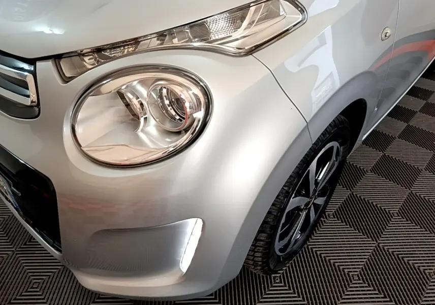 Gros plan sur l'avant droit gris clair de la Citroën C1 2019, mettant en valeur le phare rond et la roue noire.