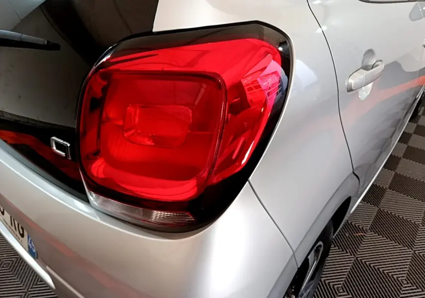 Gros plan sur le feu arrière droit rouge d'une Citroën C1 gris clair, vue trois quarts arrière droit.