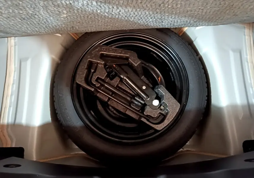 Gros plan sur la roue de secours et le kit d'outils dans le coffre d'une Citroën C1 gris clair.