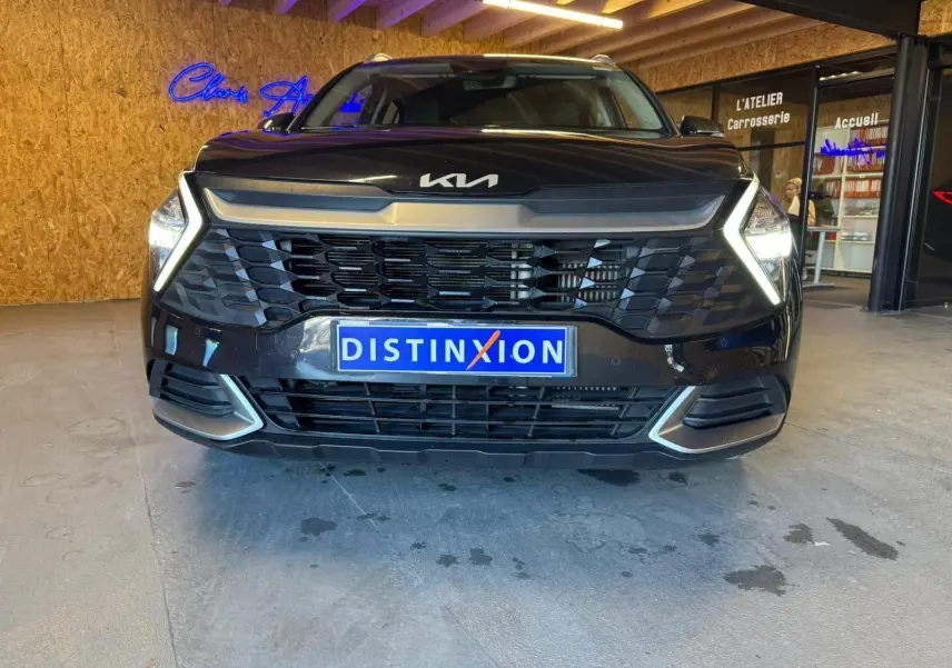 Vue avant d’un KIA Sportage noir 2022 avec calandre imposante et phares allumés dans un garage.