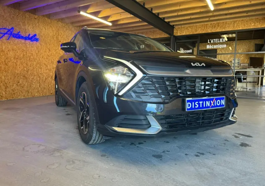Vue 3/4 avant gauche d’un KIA SPORTAGE noir 2022 avec calandre distinctive et feux allumés en intérieur showroom.