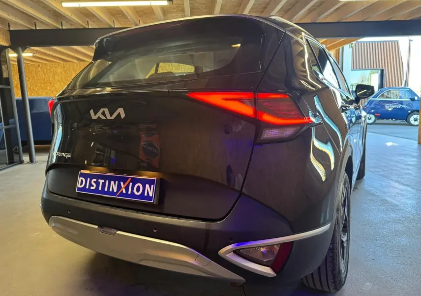 Vue 3/4 arrière droite d’un KIA Sportage noir 2022 avec feux arrière allumés et détails chromés sur le pare-chocs.