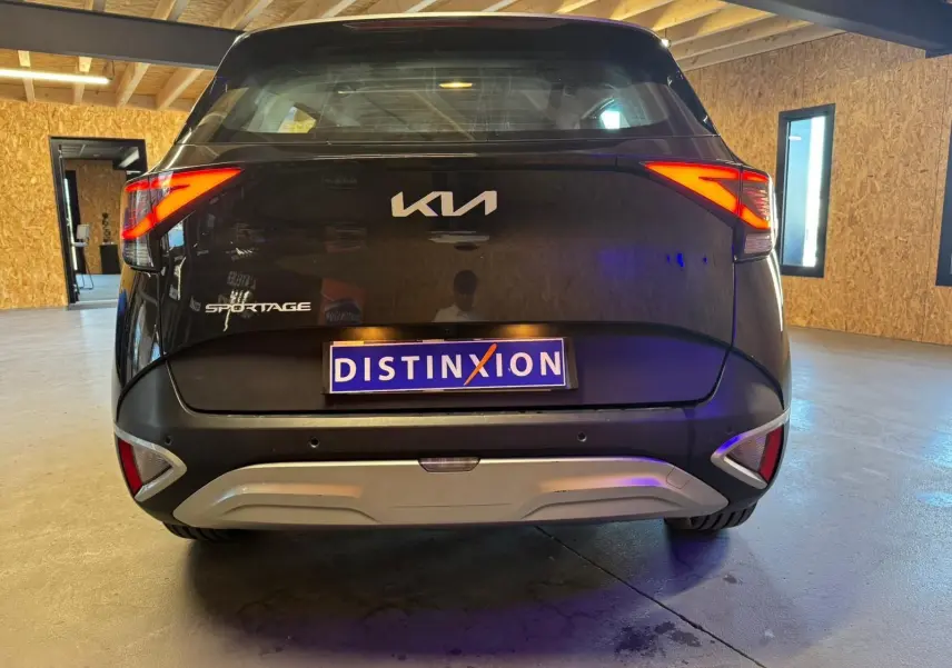Vue arrière d’un KIA Sportage noir 2022 avec feux arrière allumés et plaque d’immatriculation Distinxion.