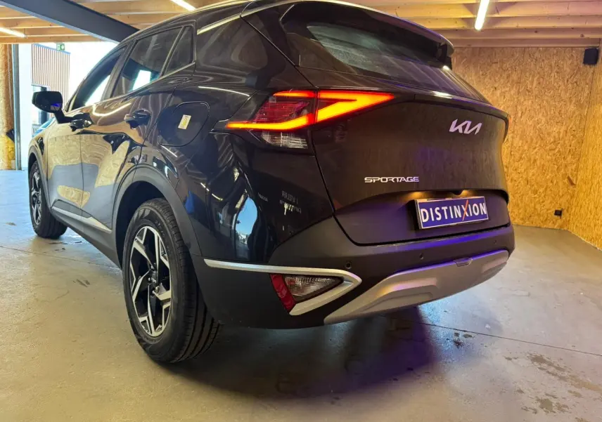 Vue 3/4 arrière droite d'un KIA Sportage noir 2022 avec feux arrière allumés et jantes alliage distinctives.