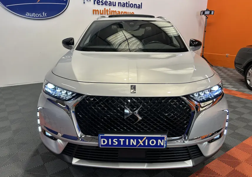 Vue avant frontale du DS7 Crossback bleu cristal avec calandre noire et phares LED allumés en intérieur showroom.