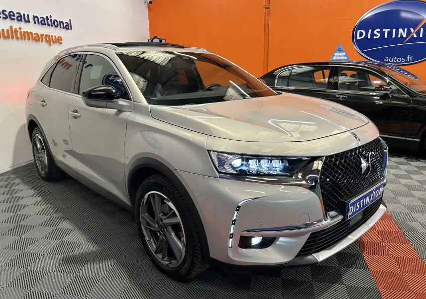 DS7 Crossback bleu clair en 3/4 avant droit, avec calandre distinctive et feux LED allumés dans un showroom.
