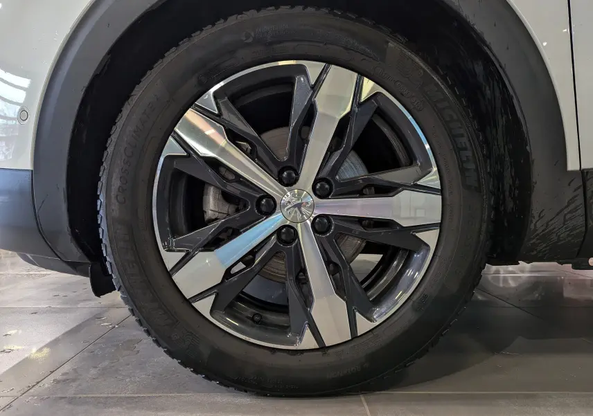 Gros plan sur la roue avant droite d'un Peugeot 3008 blanc Glacier, jante alliage bicolore au design moderne.