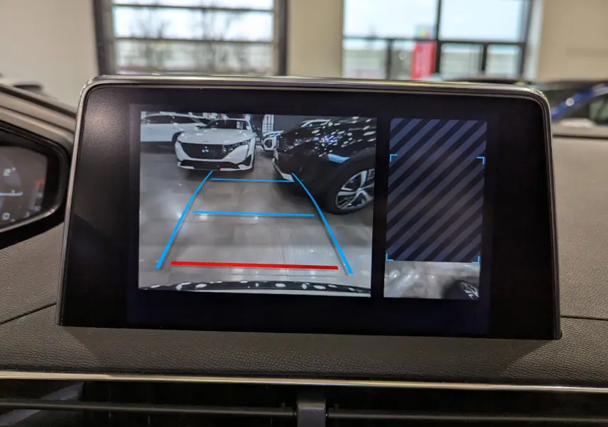 Écran de caméra de recul du Peugeot 3008 blanc Glacier avec toit noir, montrant une voiture garée en face dans un parking intérieur.
