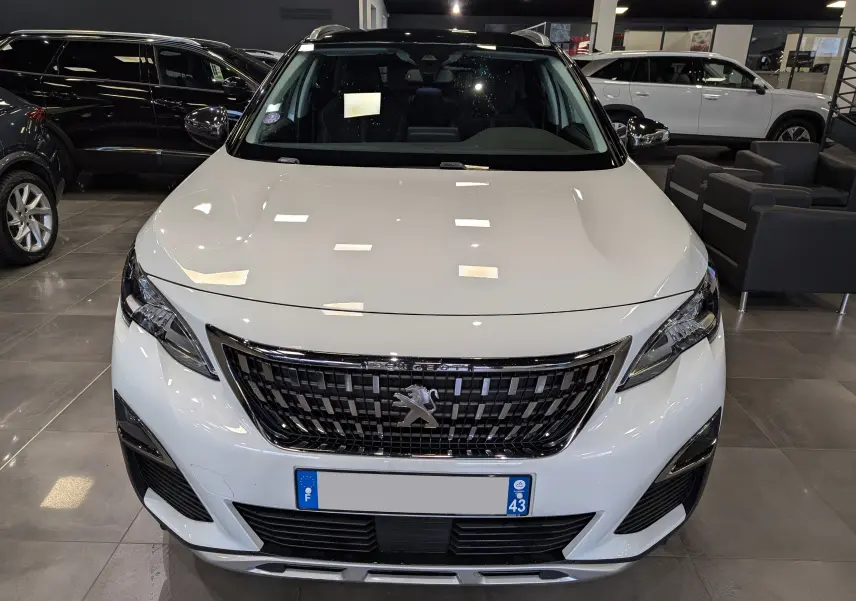 Vue de face d'un Peugeot 3008 blanc Glacier avec toit noir, en showroom, soulignant sa calandre distinctive.