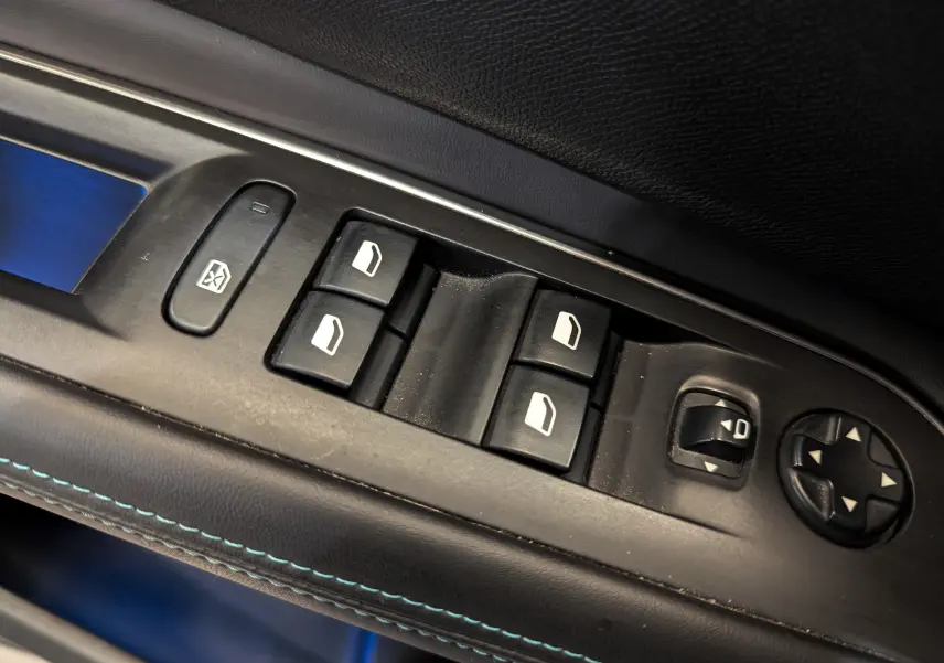 Gros plan sur les commandes de lève-vitres et réglages des rétroviseurs côté conducteur du Peugeot 3008 blanc Glacier avec surpiqûres bleues.