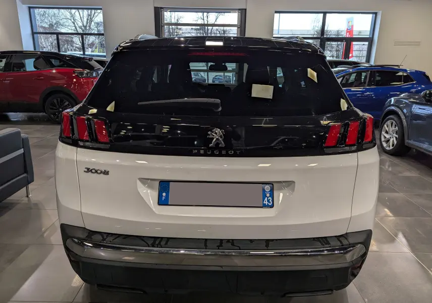 Vue arrière d'un Peugeot 3008 blanc Glacier avec toit noir, dans un showroom lumineux, mettant en valeur ses feux arrière distinctifs.