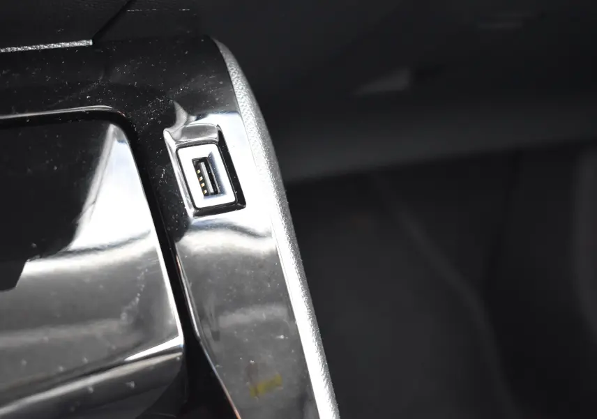 Gros plan sur un port USB intégré dans la console centrale noire brillante d'un Peugeot 2008 bleu 2021.