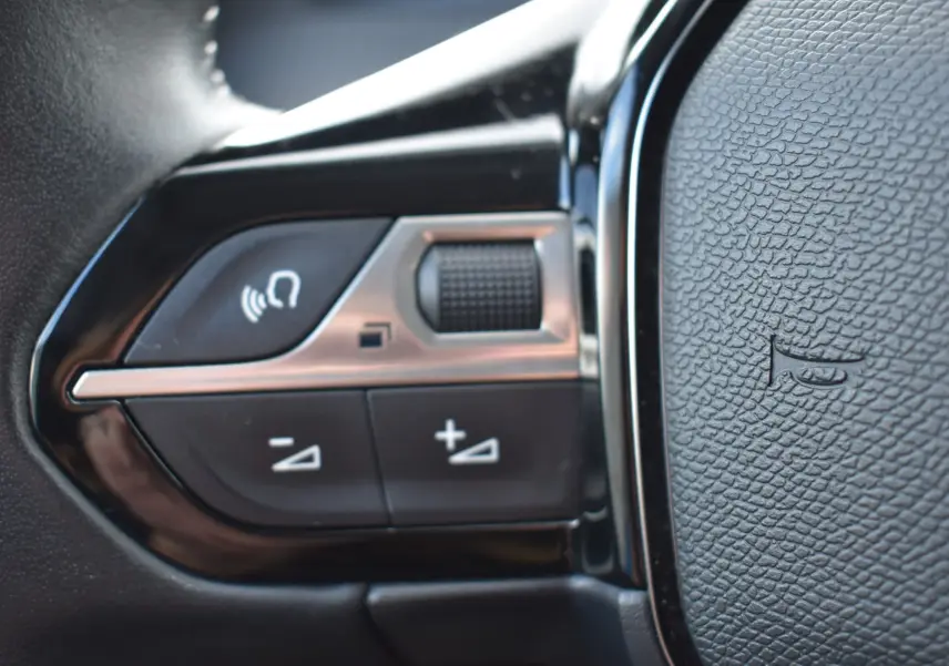 Détail des commandes au volant noir du Peugeot 2008 2021 BlueHDi 110 Allure, avec boutons de volume et micro.