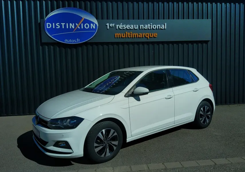 Volkswagen Polo blanc vue 3/4 avant droit, stationnée devant un mur noir avec enseigne Distinxion.