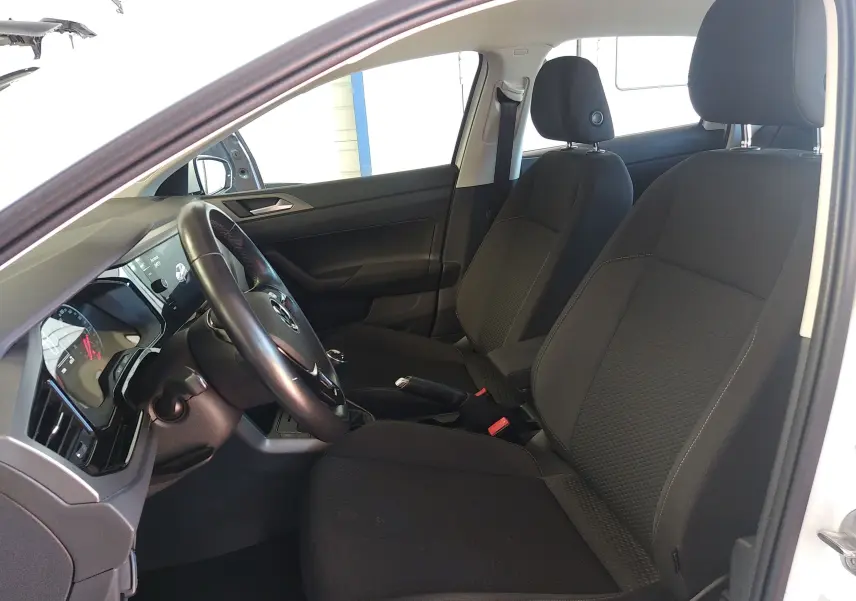 Vue intérieure côté conducteur de la Volkswagen Polo blanche 2021, montrant les sièges noirs et le tableau de bord moderne.