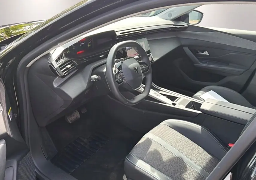 Vue intérieure côté conducteur de la Peugeot 408 Hybrid noire 2024, avec volant cuir et console centrale moderne.