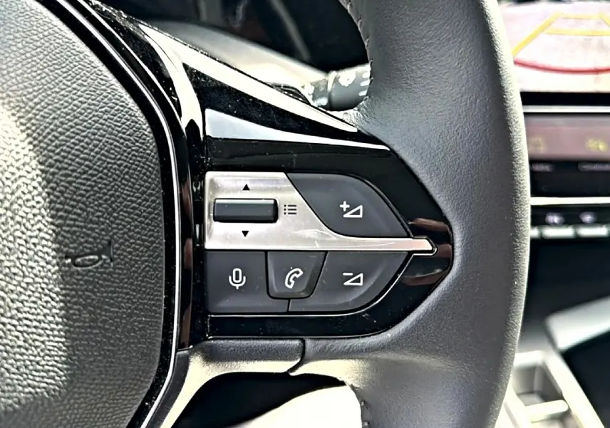 Gros plan sur les commandes vocales et téléphone du volant cuir côté gauche d’une Peugeot 408 Hybrid 2024 noire.