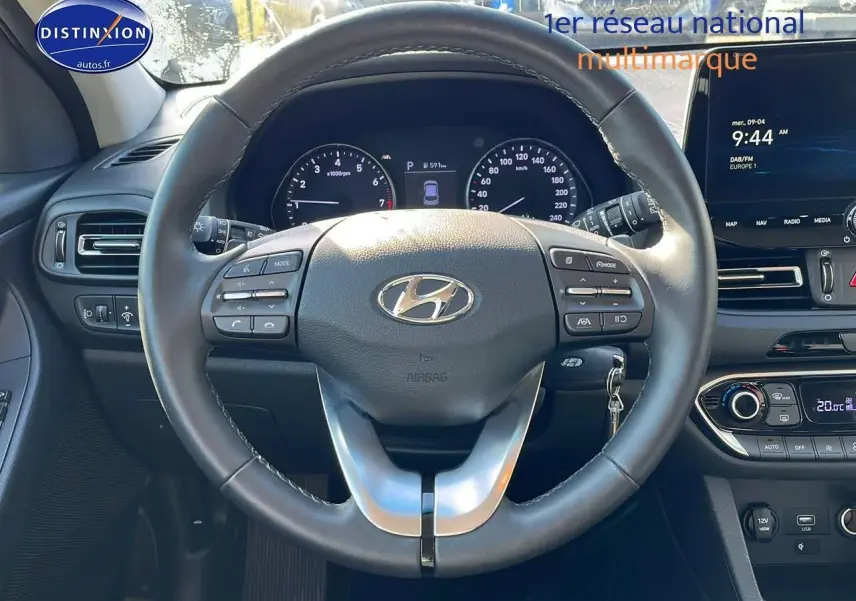 Vue centrée sur le volant cuir multifonction d'une Hyundai i30 gris argent 2024 avec tableau de bord et écran tactile visible.