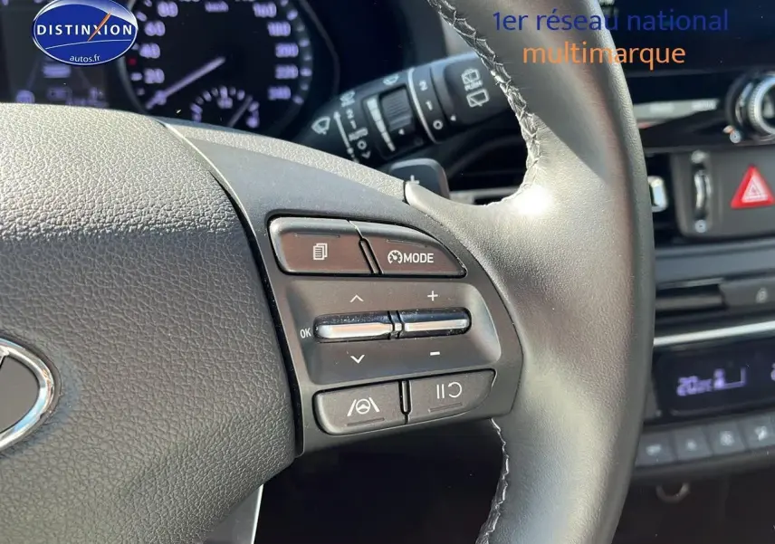 Gros plan sur le volant cuir multifonction gris d'une Hyundai i30 2024 avec commandes de régulateur et tableau de bord flou.