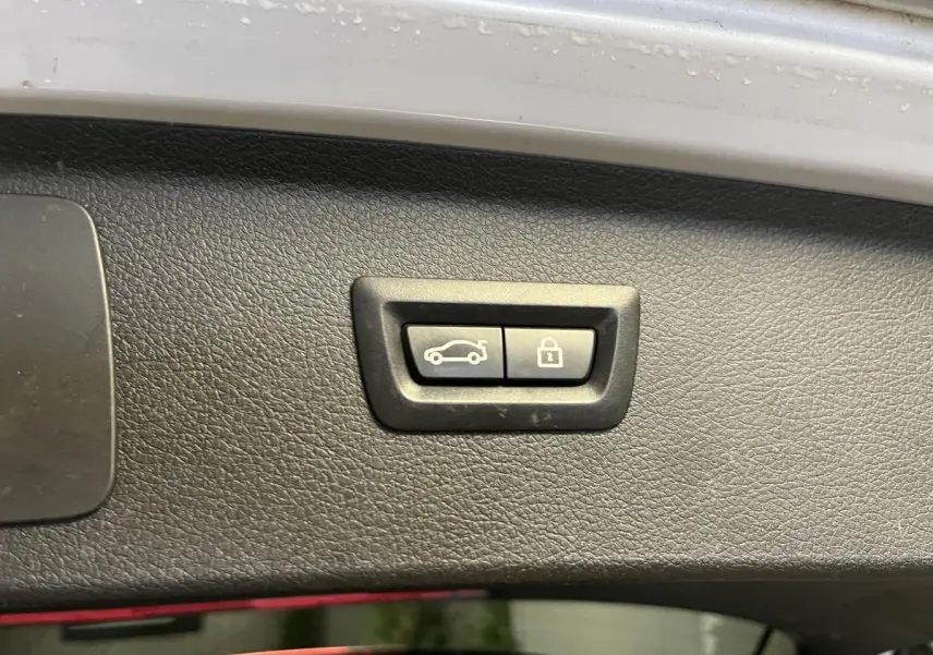 Gros plan sur les boutons d'ouverture et de verrouillage du hayon du BMW Série 2 225xe gris, vue intérieure du coffre.