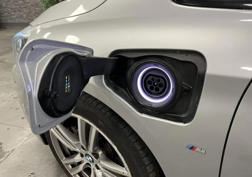 Prise de recharge ouverte côté avant gauche sur BMW Série 2 gris avec jante alliage et badge M visible.