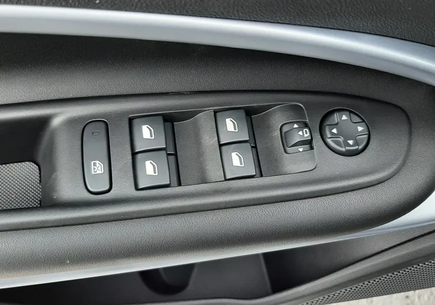 Gros plan sur les commandes de lève-vitres et réglages des rétroviseurs côté conducteur du Jeep Avenger 2025, intérieur noir.