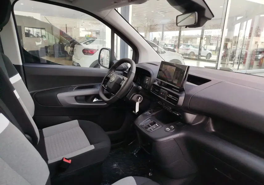 Vue intérieure côté conducteur du Citroën Berlingo 2025, sièges gris, tableau de bord avec écran tactile et volant multifonction.