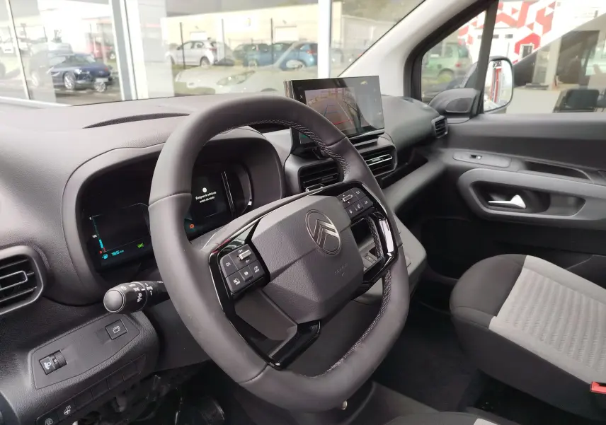 Vue intérieure côté conducteur du Citroën Berlingo 2025, tableau de bord noir avec écran central et volant multifonction.