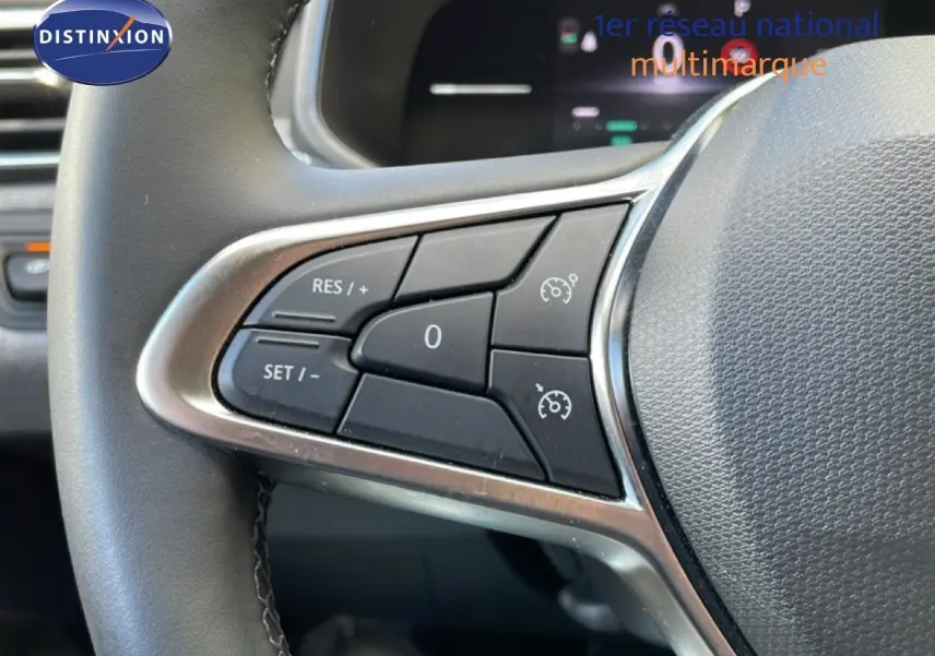 Gros plan sur les commandes de régulateur de vitesse au volant de la Renault Clio gris schiste métal, intérieur moderne.